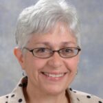 A woman with white hair and glasses smiling.